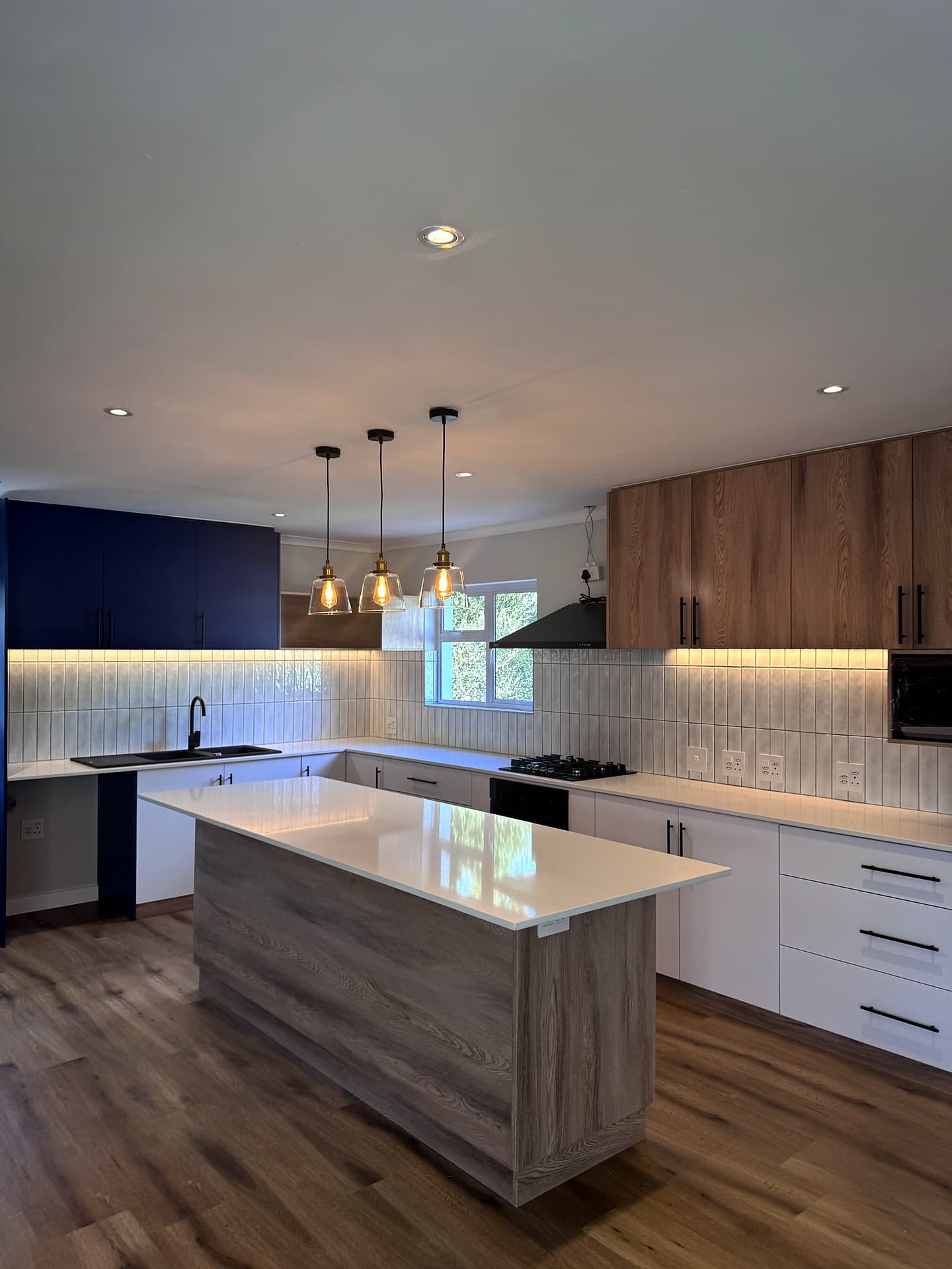 Bloubergstrand – Kitchen island with pendants above, oak units and a navy feature wall