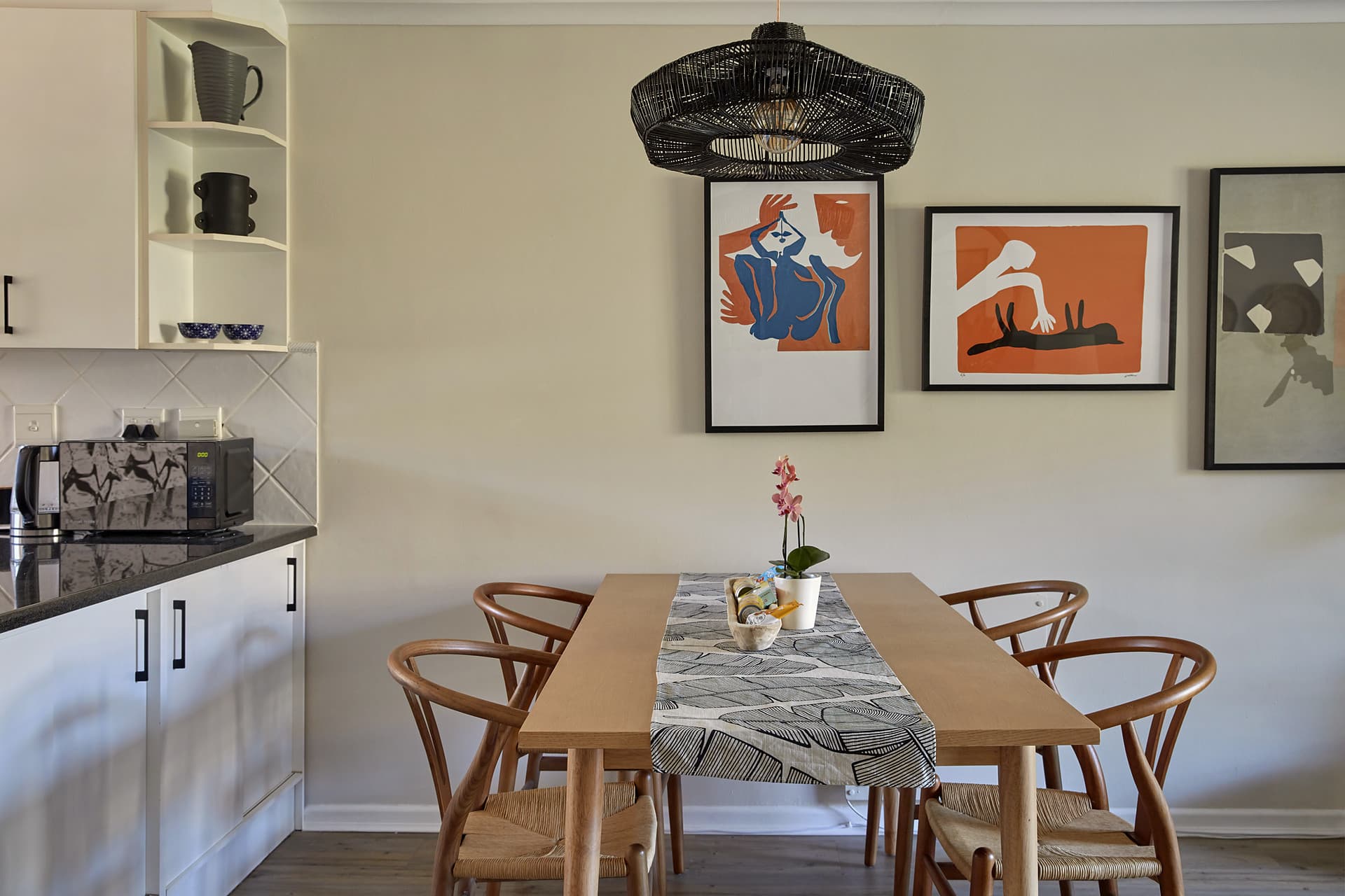 Gardens – Dining table and wishbone chairs beside the kitchen counter, with open shelving and framed prints on the wall