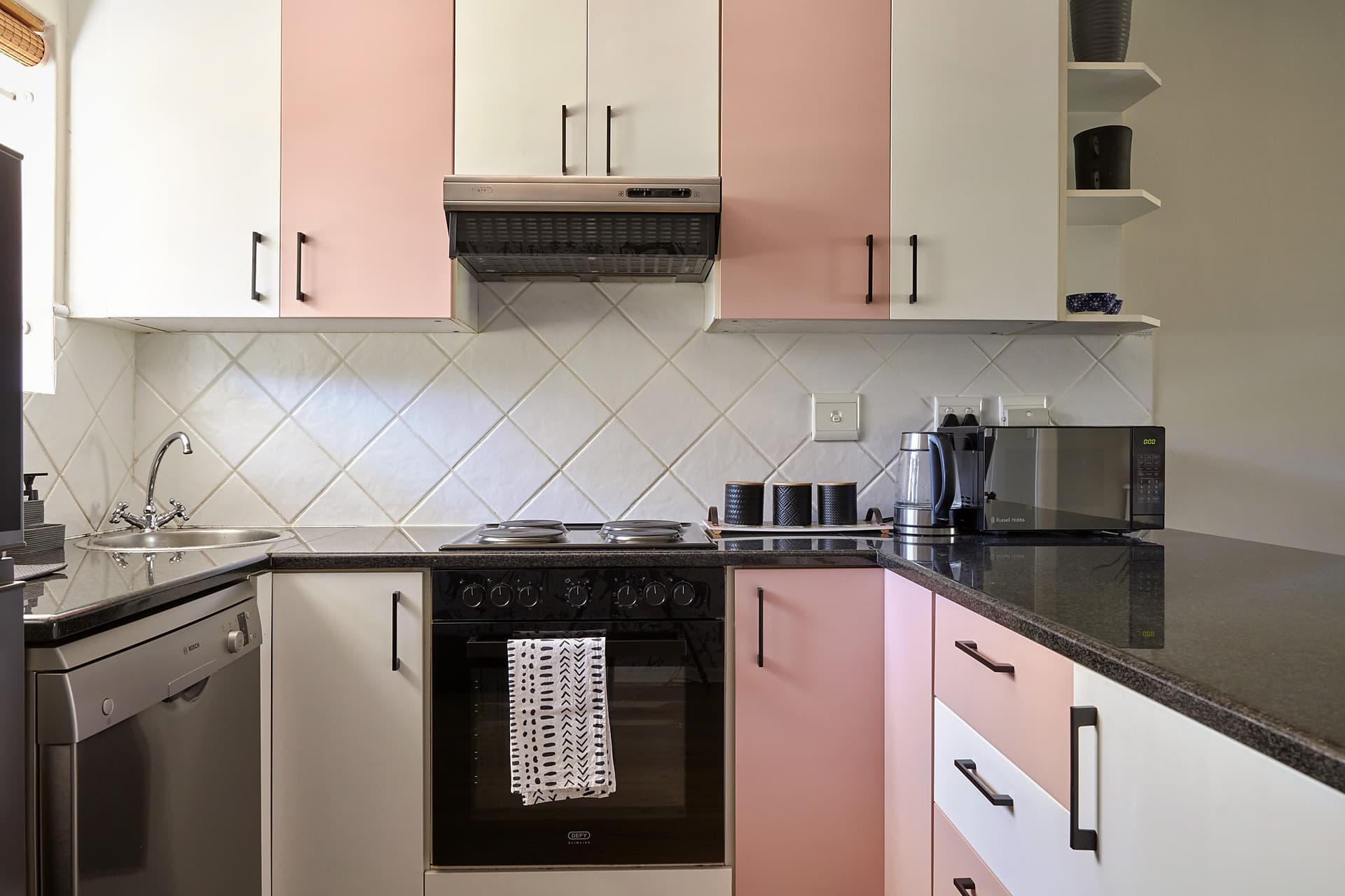 Gardens – Kitchen with pink and cream cabinet fronts, a diamond-tiled splashback and dark granite worktops