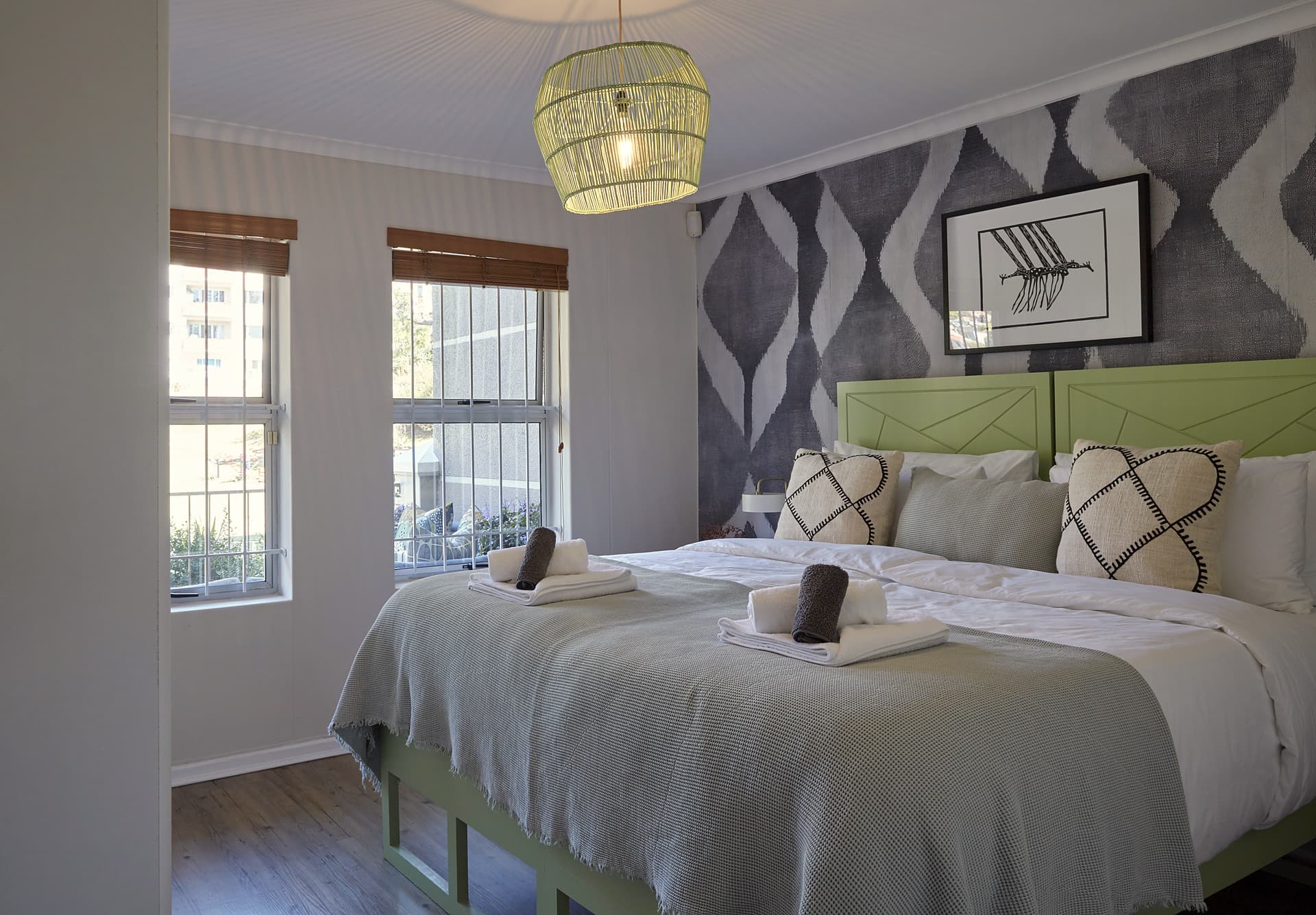 Gardens – Main bedroom with a green painted headboard, an ikat-patterned feature wall and a green woven pendant