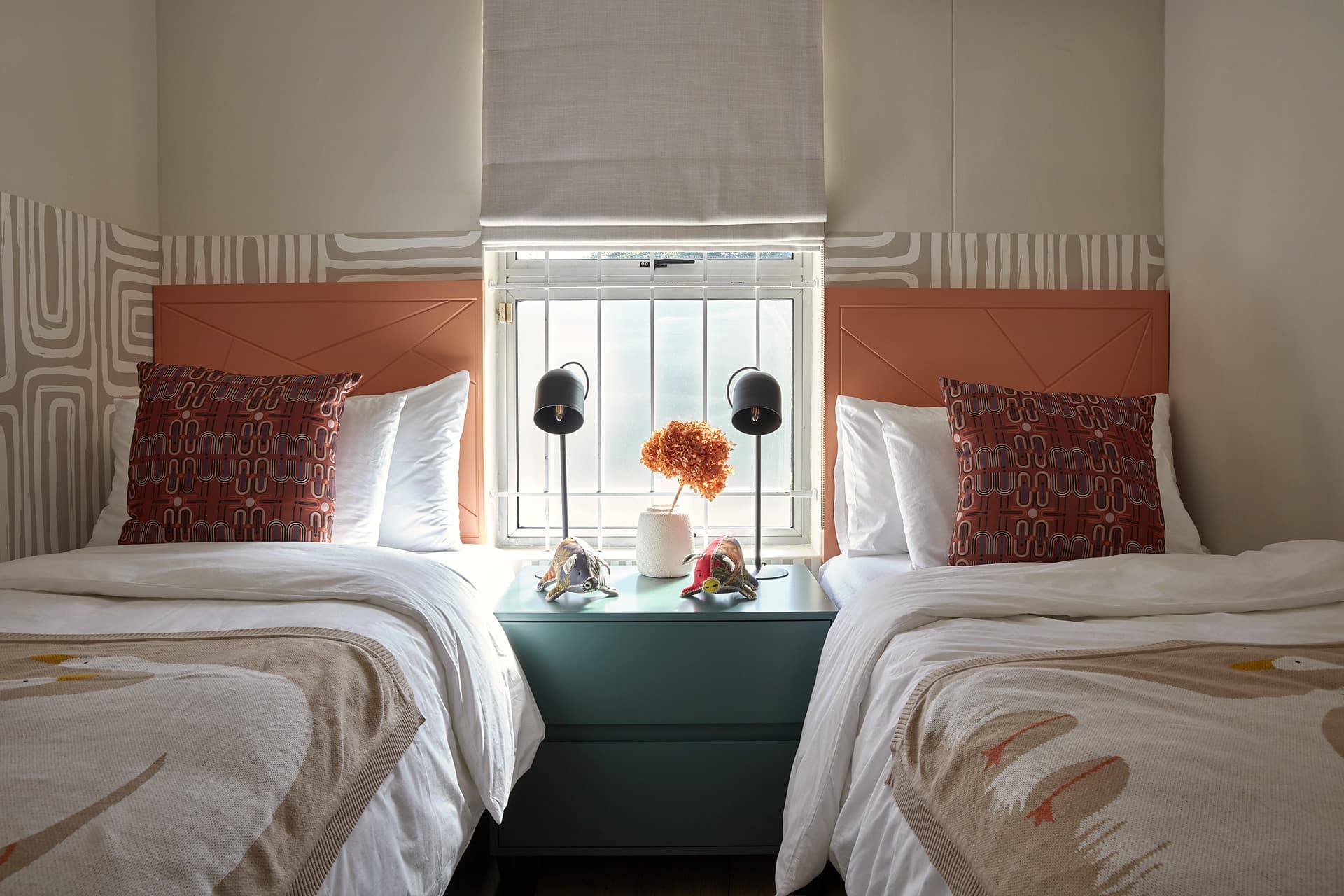 Gardens – Twin beds either side of a green bedside chest beneath the window, with wall lamps and patterned cushions