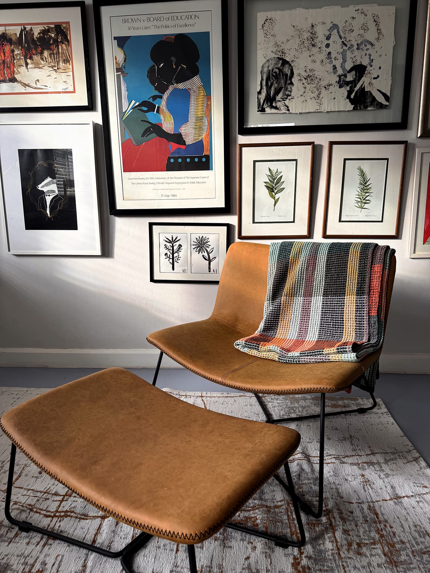 Mowbray – Tan leather chair and ottoman with a striped throw beneath a gallery wall of framed prints