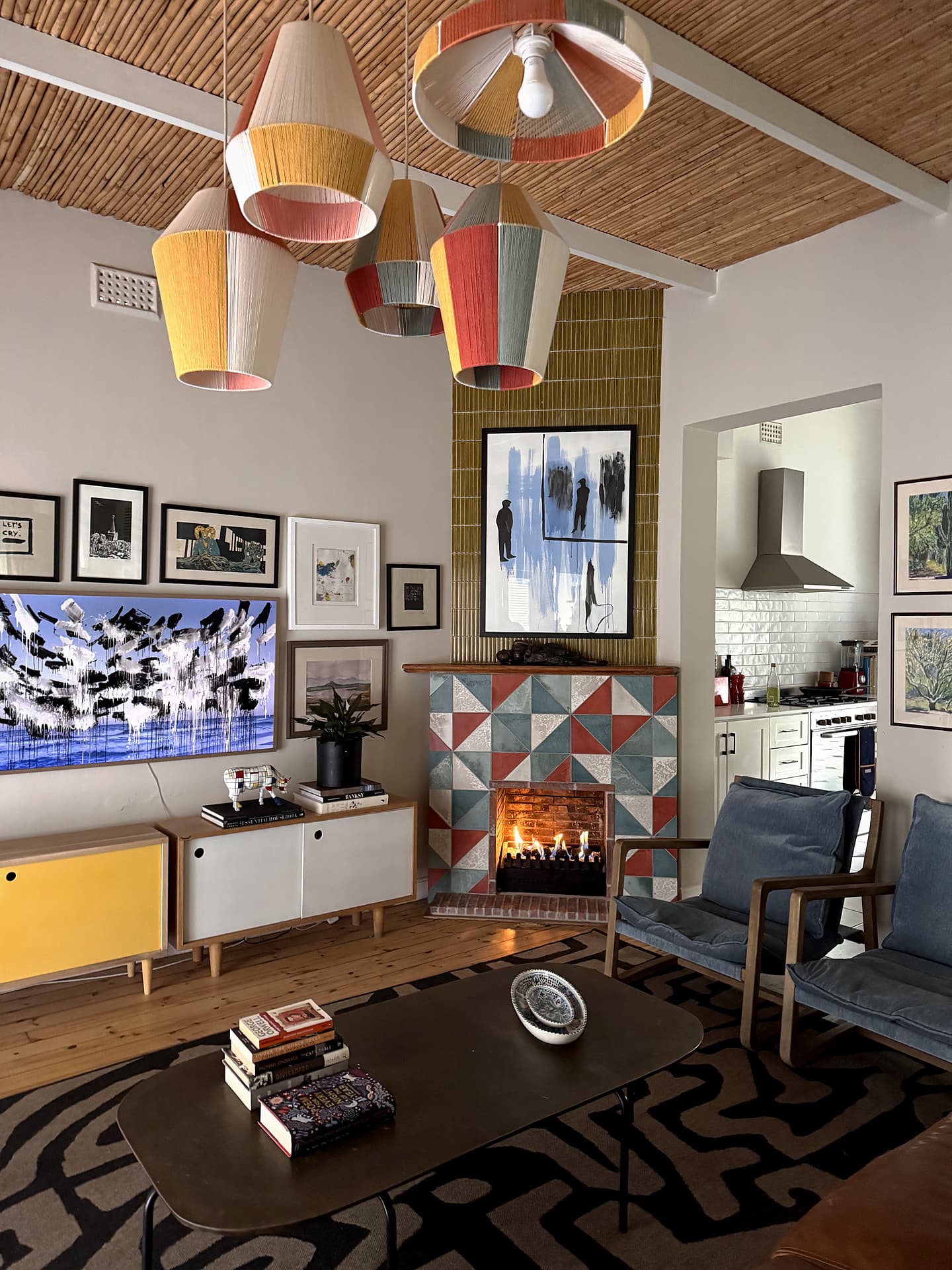 Mowbray – Living room with woven pendants, a tiled fireplace lit, gallery wall and a patterned rug