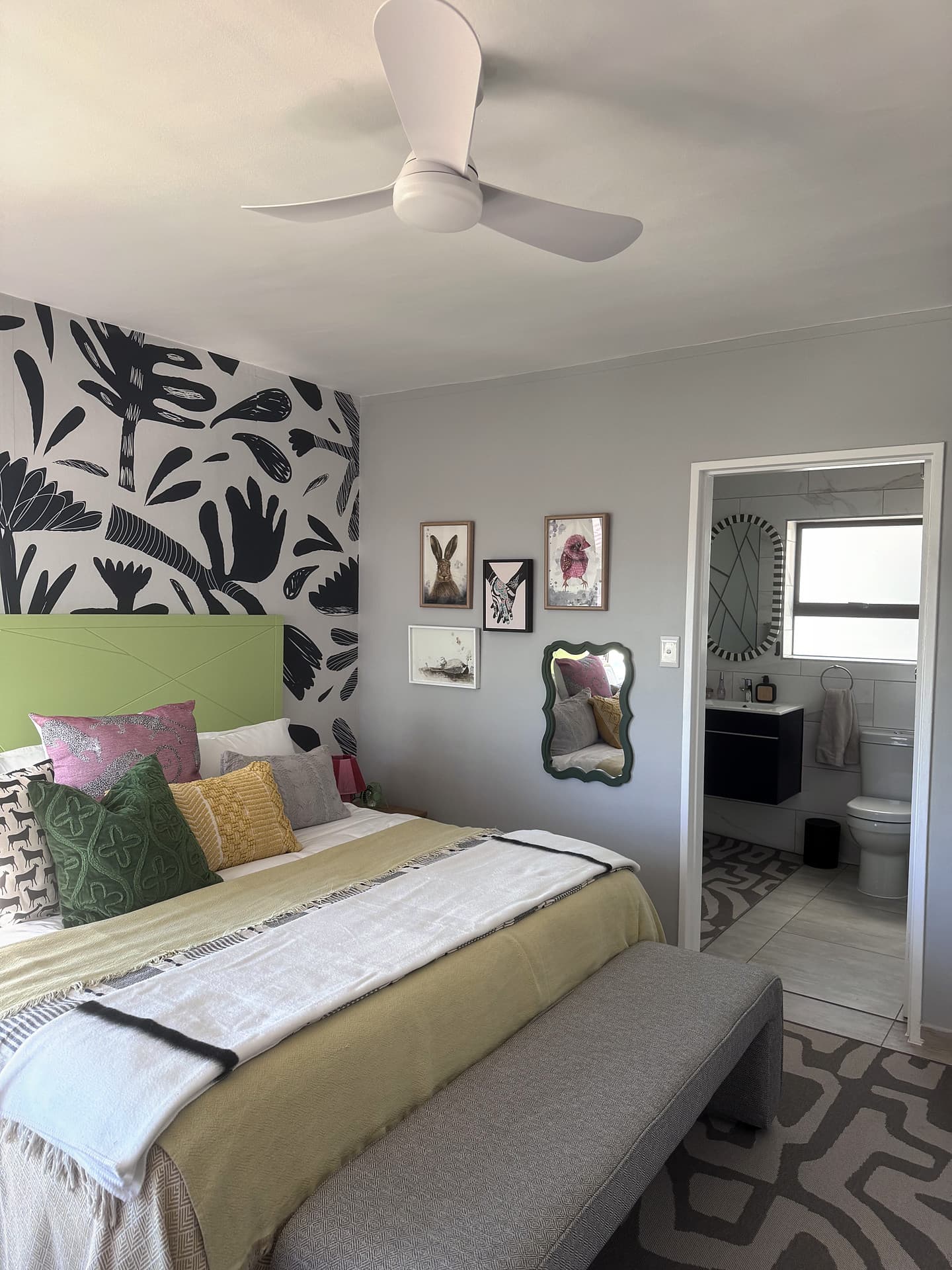 Strand – Bedroom with a green headboard and navy leaf mural, door open to the en-suite