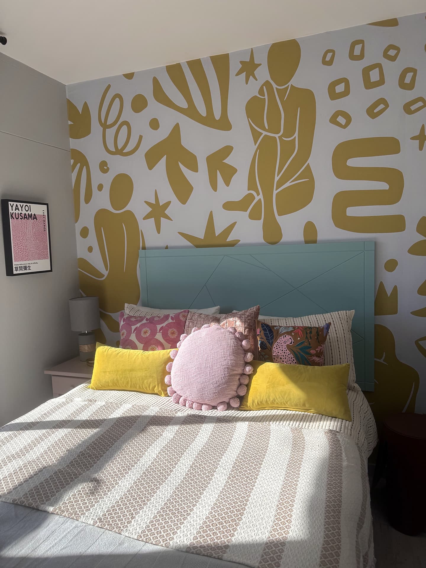 Strand – Bed with a teal headboard, mustard mural and a Kusama print