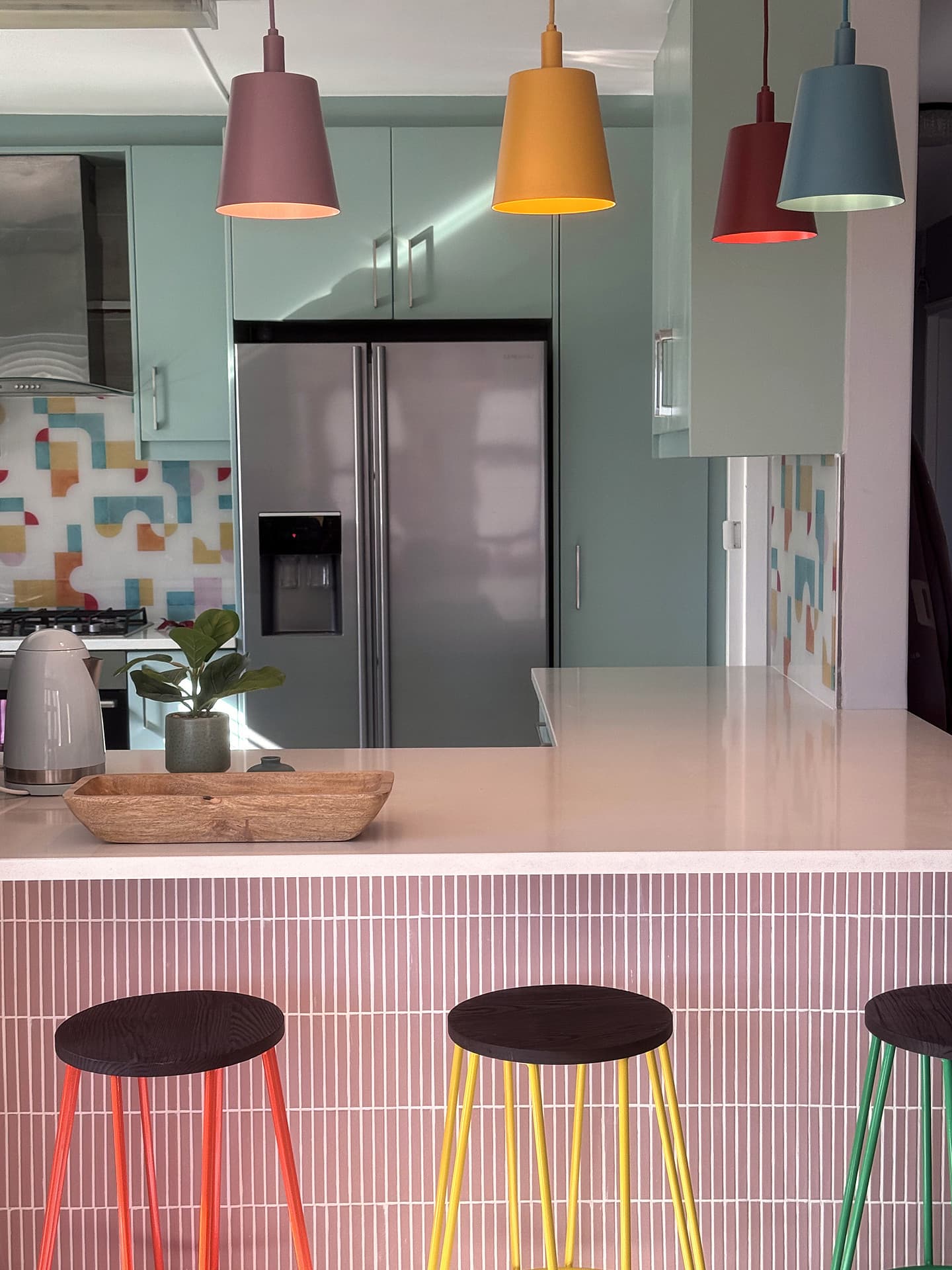 Strand – Pink tiled kitchen island with three coloured hairpin stools and pendants