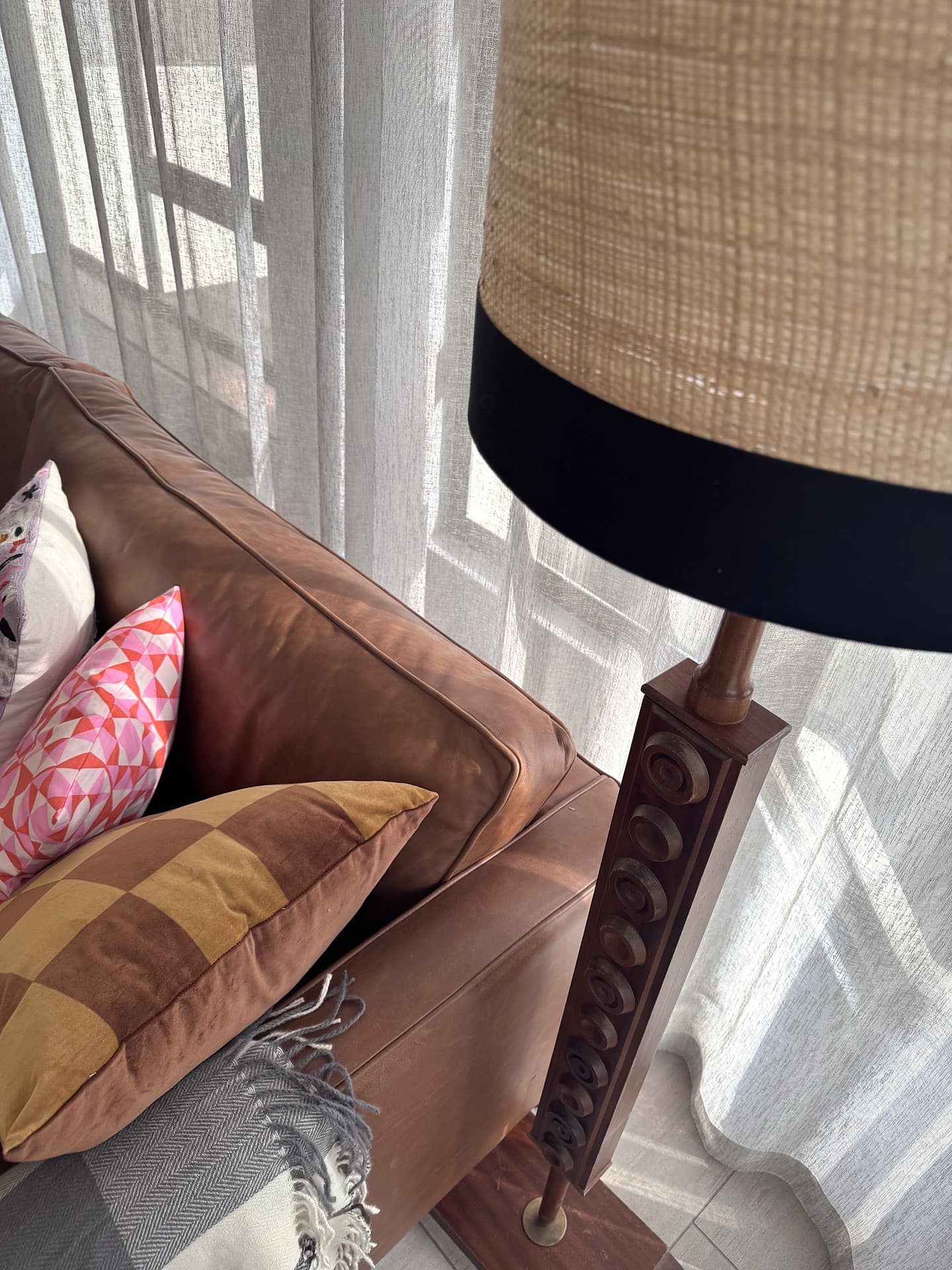 Strand – Leather sofa, cushions and a rattan lamp shade in front of sheer curtains