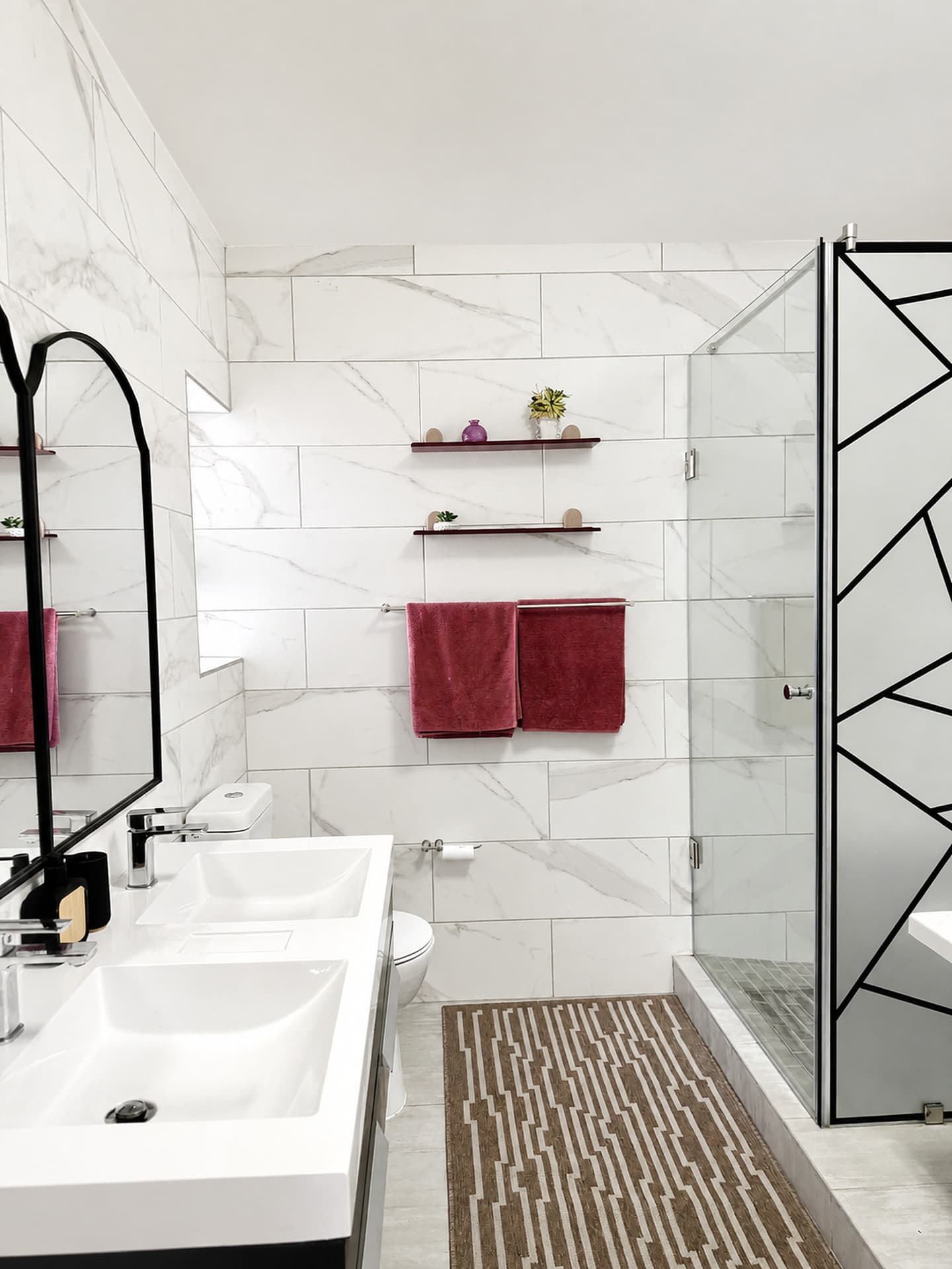 Strand – Main bathroom with a double basin, burgundy towels and a black-line shower screen