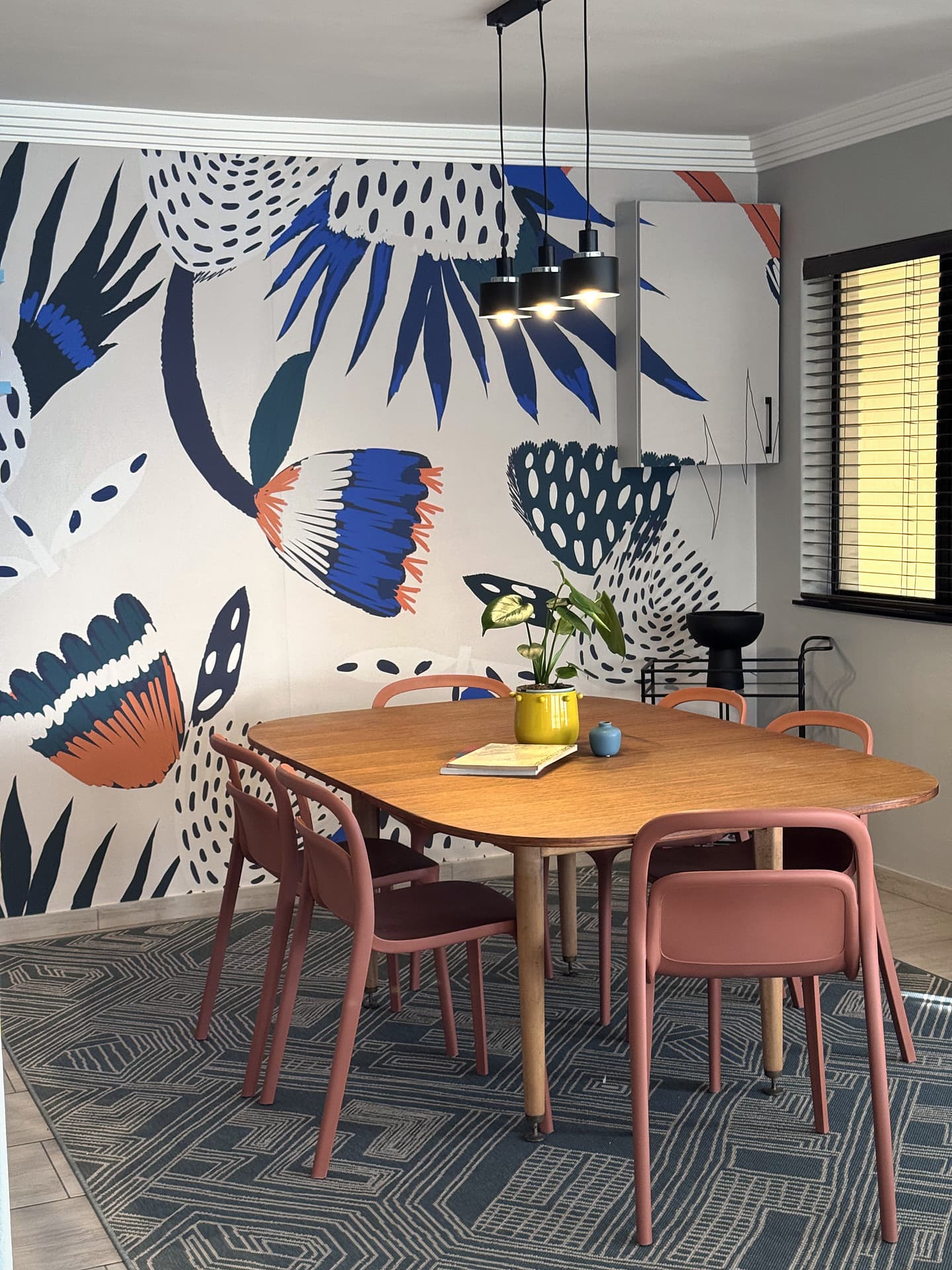 Strand – Dining table and chairs against the blue floral mural