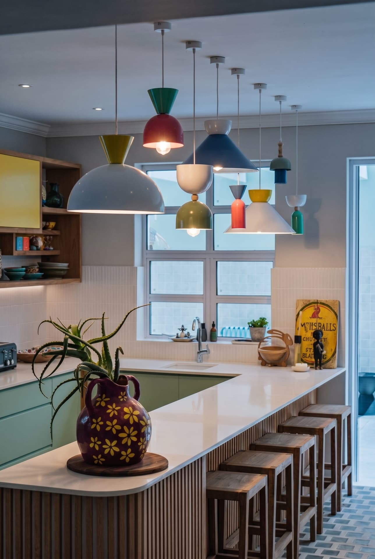 The Kalk Bay kitchen: a cluster of coloured pendant lights over a timber-slat island, yellow-panelled joinery and open shelves