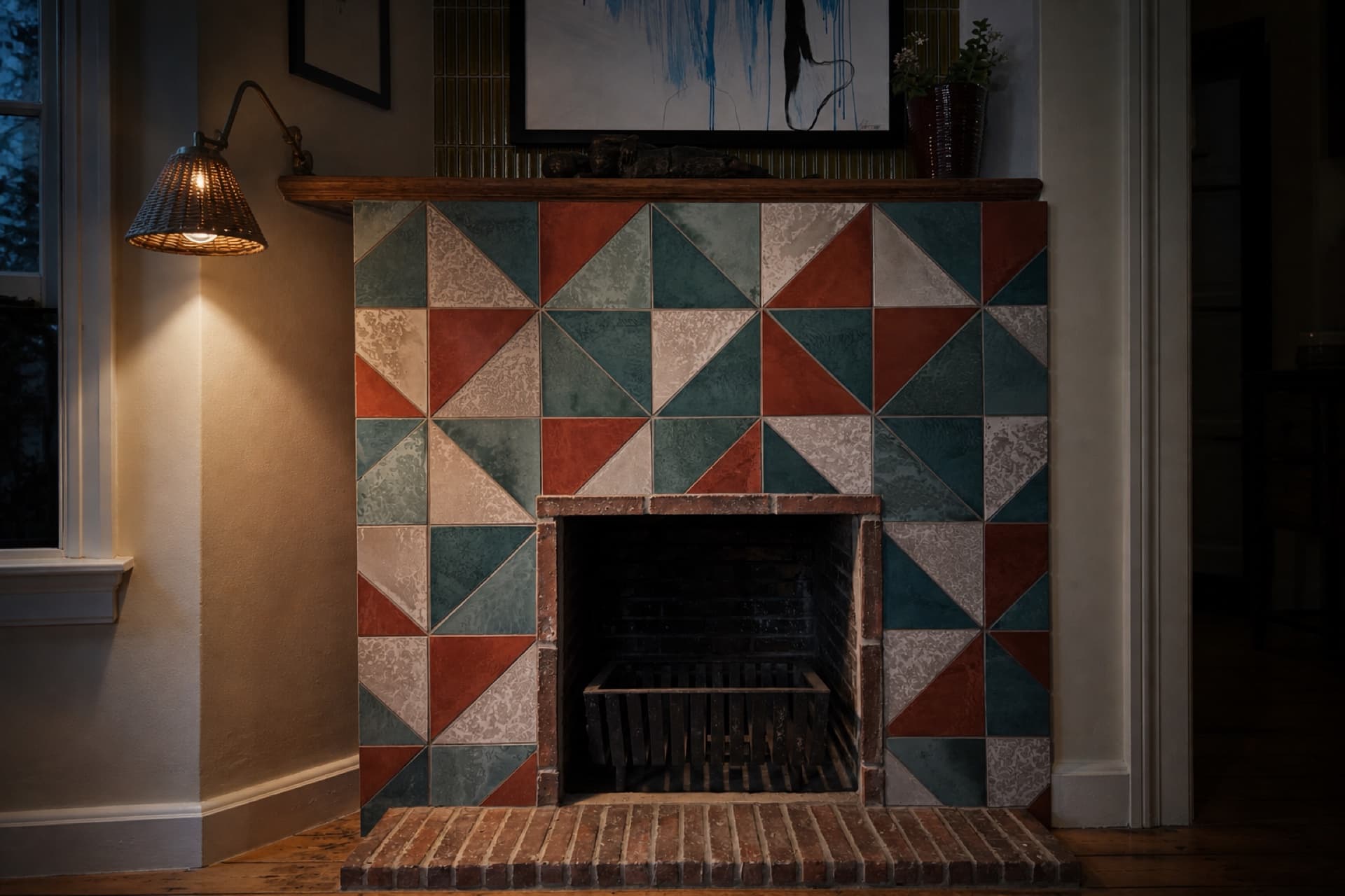 The Mowbray fireplace: hand-made triangular tiles in rust, teal and bone under lamplight, on a brick hearth
